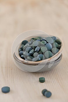 Spirulina algae green in tablets in ceramic cups on a light wooden shabby background..Dietary supplements.Super food