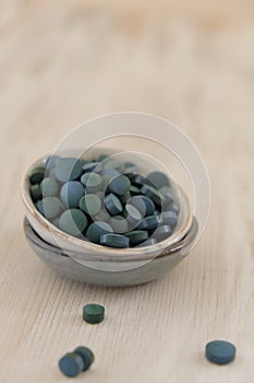Spirulina algae green in tablets in round ceramic cups on a light wooden background..Dietary supplements.Super food