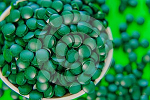 Spirulina algae tablets.Spirulina pills in a round bowl.Green spirulina tablets on green background. dietary supplements