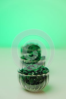 Spirulina algae tablets in transparent cups in a row on a light green background.Green spirulina tablets. Vitamins and