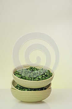 Spirulina pills in a green cups set on a light background with reflection.Vitamins and dietary supplements.Spirulina
