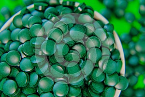 Spirulina pills in a round bowl. Green spirulina tablets on green background.Spirulina algae tablets. Super food .Food