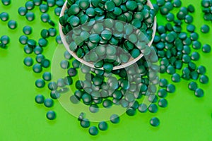 Spirulina pills in a round bowl.Green spirulina tablets on green background. Vitamins and dietary supplements