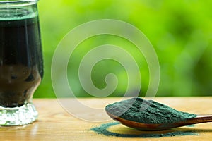 Spirulina powder in wooden spoon and green smoothie with spirulina on wood background