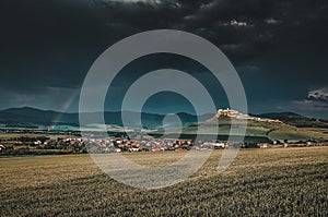 Spis castle in spring and rainbow - agricultural field with green wheat in foreground