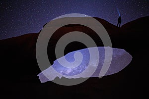 Spitzkoppe national park in Namibia. Gazing the stars on Natural Rock Arch, woman with focused beam of headlamp pointing directly