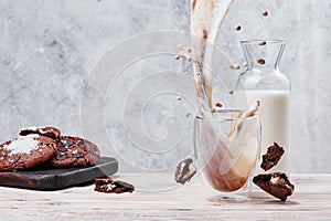 Splash of coffee with milk in a transparent glass. Chocolate cookies and glass of milk on light concrete background photo