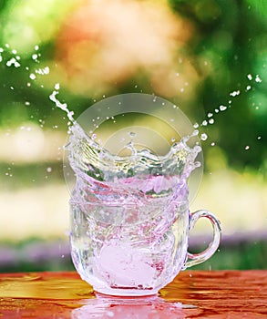 Splash of cool fresh water with ice cube in transparent glass cup in the table outoors in summer day.