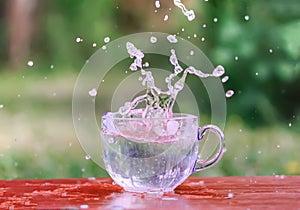 Splash of cool fresh water with ice cube in transparent glass cup in the table outoors in summer day.
