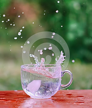 Splash of cool fresh water with ice cube in transparent glass cup in the table outoors in summer day.