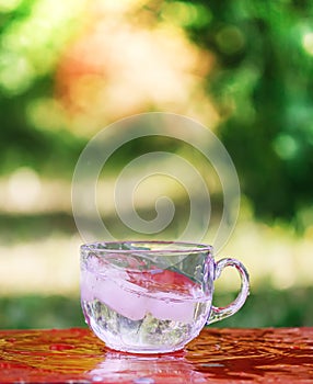 Splash of cool fresh water with ice cube in transparent glass cup in the table outoors in summer day.