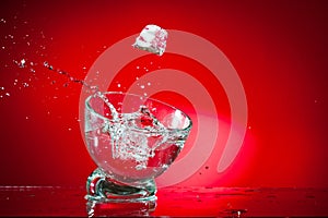 A splash of a drink in a glass from an ice cube falling into it, shot against a bright red background