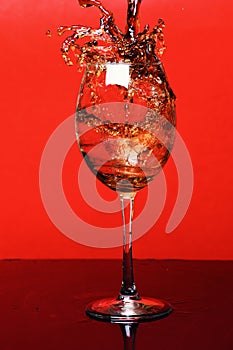 Splash of drink in wine glass on red background, side vie