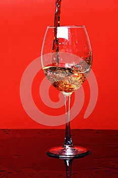 Splash of drink in wine glass on red background, side vie