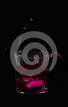 Splash from ice cube in a glass of red water or drink