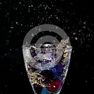 splash of liquid in rainbow sparkling glass with cherries on black background, low key