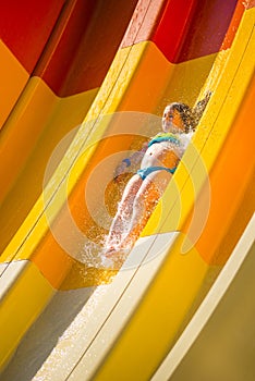 Splash. Little caucasian girl on water slide of water park. Sunny summer day