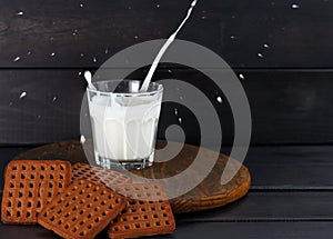 splash of milk glass with chocolate cookies on dark wooden background