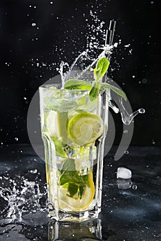 Splash of mojito cocktail or lemonade with lime and mint in glass on black. Close up. Summer drink