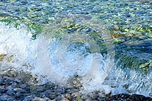 A splash of pure turquoise sea wave on pebble on the seashore