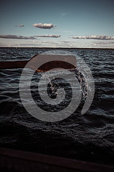 Splash from rowing wooden oar on boat on a lake during sunny day