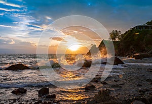 Splash sea waves on rock beach with sunset rain clouds sky with light flare