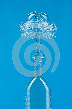 A splash of water with drops escaping from a PET bottle on a blue background. The concept of pure bottled water