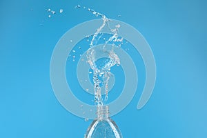 A splash of water with drops escaping from a PET bottle on a blue background. The concept of pure bottled water