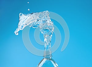 A splash of water with drops escaping from a PET bottle on a blue background. The concept of pure bottled water