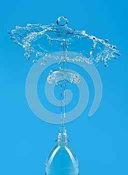A splash of water with drops escaping from a PET bottle on a blue background. The concept of pure bottled water