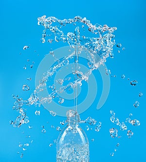 A splash of water with drops escaping from a PET bottle on a blue background. The concept of pure bottled water