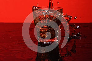 Splash of water in glass for whiskey on red background, side vie
