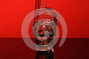 Splash of water in glass for whiskey on red background, side view.