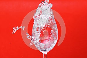 Splash of water in wine glass on red background, side vie