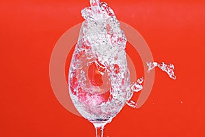 Splash of water in wine glass on red background, side vie