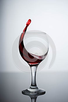 Splashes of red wine in a glass on a black glossy glass on a white background