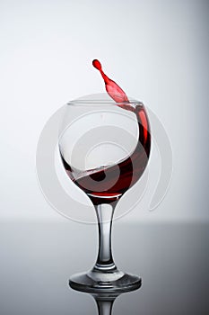 Splashes of red wine in a glass on a black glossy glass on a white background