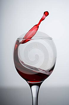 Splashes of red wine in a glass on a black glossy glass on a white background