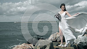 Splashes of water envelops an attractive young woman. Beautiful girl in a white dress stands on seashore