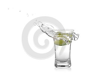 Splashing Mexican Tequila in shot glass with lime slice isolated