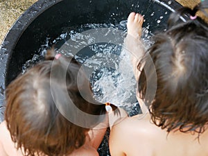 Splashing water in a bucket, as the two little Asian baby girls, sisters, playing together in a rural area of Thailand