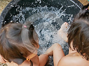 Splashing water in a bucket, as the two little Asian baby girls, sisters, playing together in a rural area of Thailand