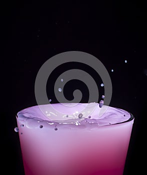 Splashing water in a glass with pink water
