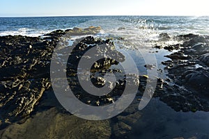 Splashing wave of turbulent sea reflected in calm water of rocky tidal pool