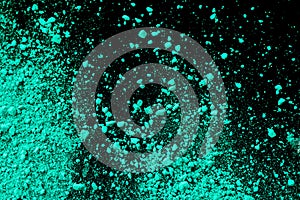 A splatter of green blue colored pigment powder on black background