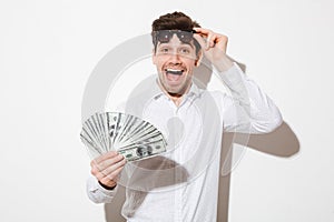 Splendid photo of excited man in shirt taking off black sunglasses and enjoying fan of money dollar bills with pleasure and