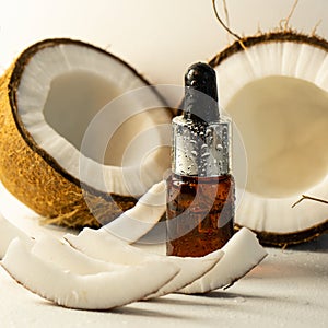 Split coconuts with coconut essential oil. Coconut serum for the face. A bottle of whey oil with a pipette on a white-beige