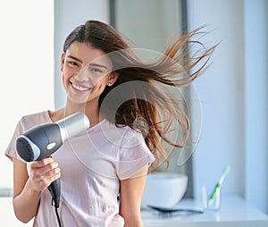 Split ends Not a chance. Cropped portrait of a beautiful young woman blowdrying her hair in the bathroom at home.