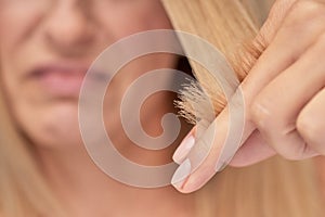 Split ends. Upset blonde woman looking at her damaged hair, selective focus