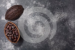 Split fermented cocoa pod with shelled cacao beans atop dark grey backdrop, top view